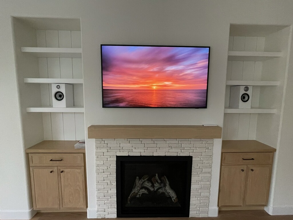 Media wall with a white stacked-stone fireplace, wood mantel, mounted TV, and flanking built-in shelving and cabinetry