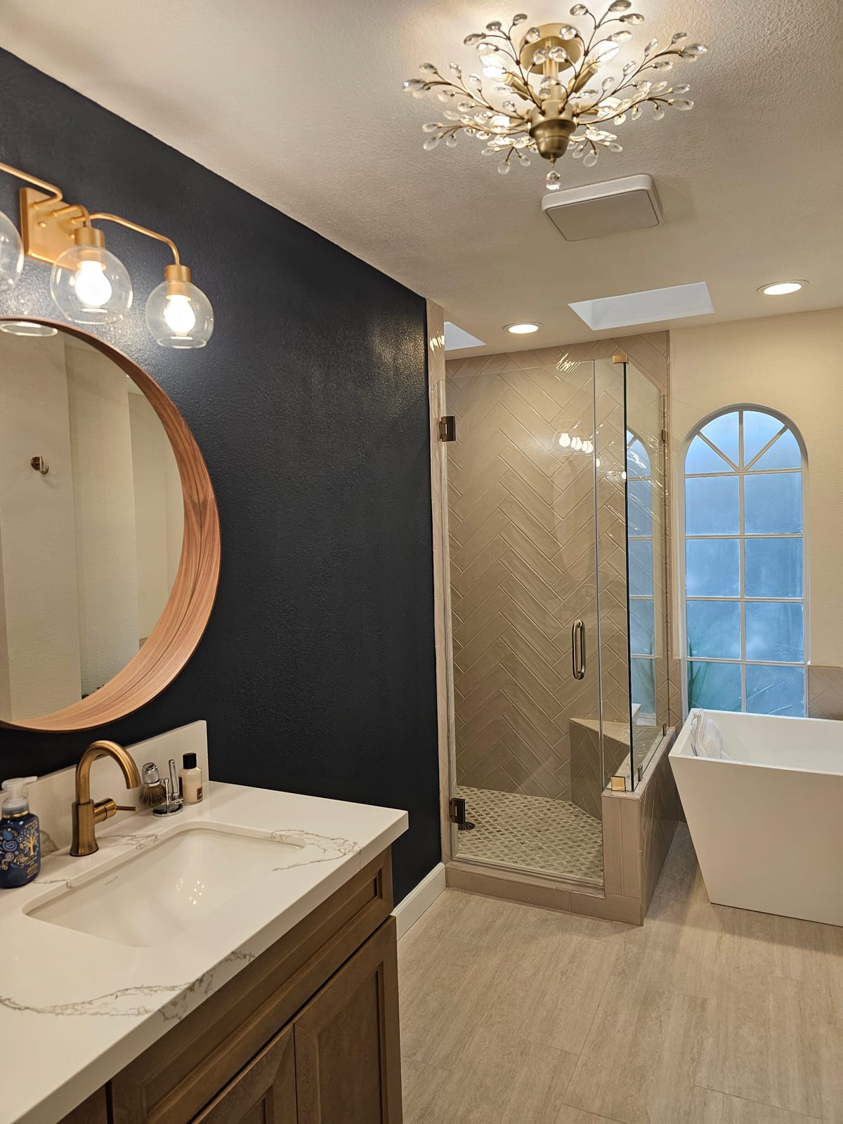 Master bathroom with navy accent wall, brass fixtures, crystal chandelier, herringbone shower, and soaking tub